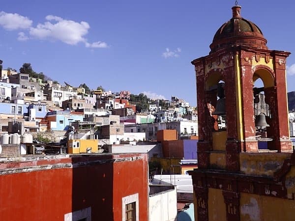 Un campanario antiguo sobre los techos, con casas de colores en el cerro al fondo