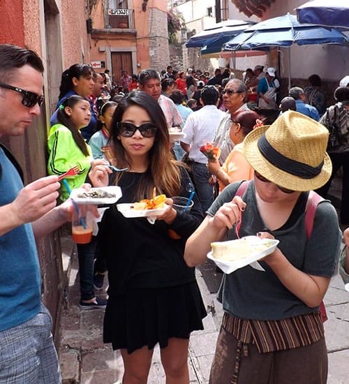 Guests eating street food from paper plates on a crowded Guanajuato street